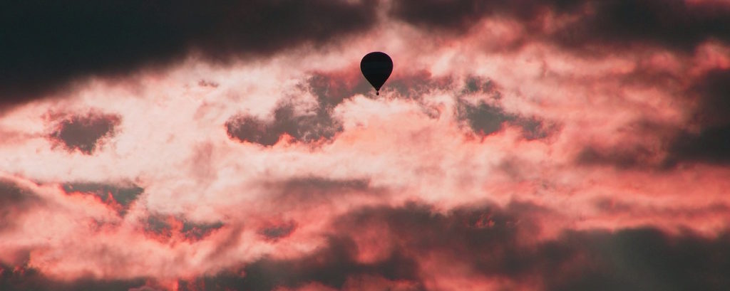 A silhouette of a hot air balloon against a pink, cloudy sky.