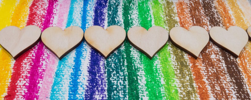 Cut-out wooden hearts laying against a rainbow background.