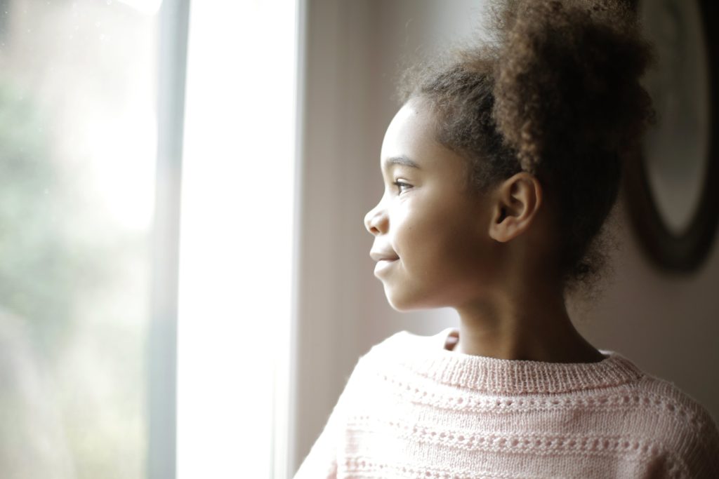 A photo of a young girl staring out the window with a pleasant expression.
