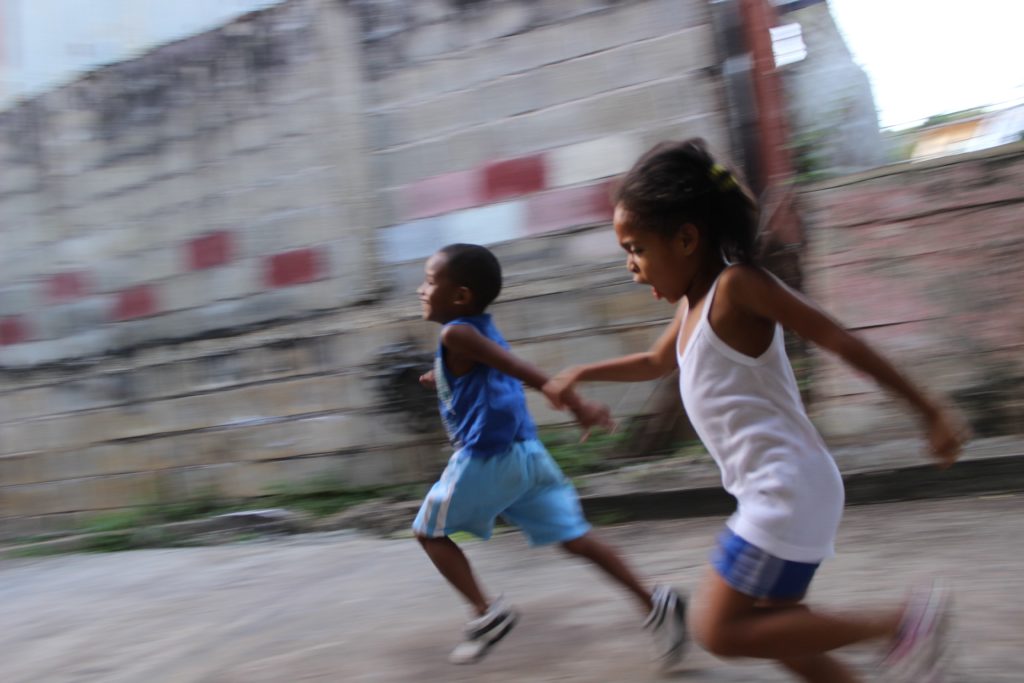 Two kids running down a street. The photo has a motion blur effect to capture their movement.
